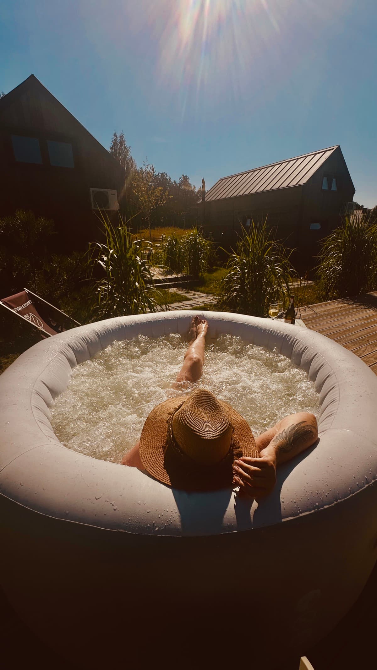 Relaks w jacuzzi — kapelusz, wino i domki w tle